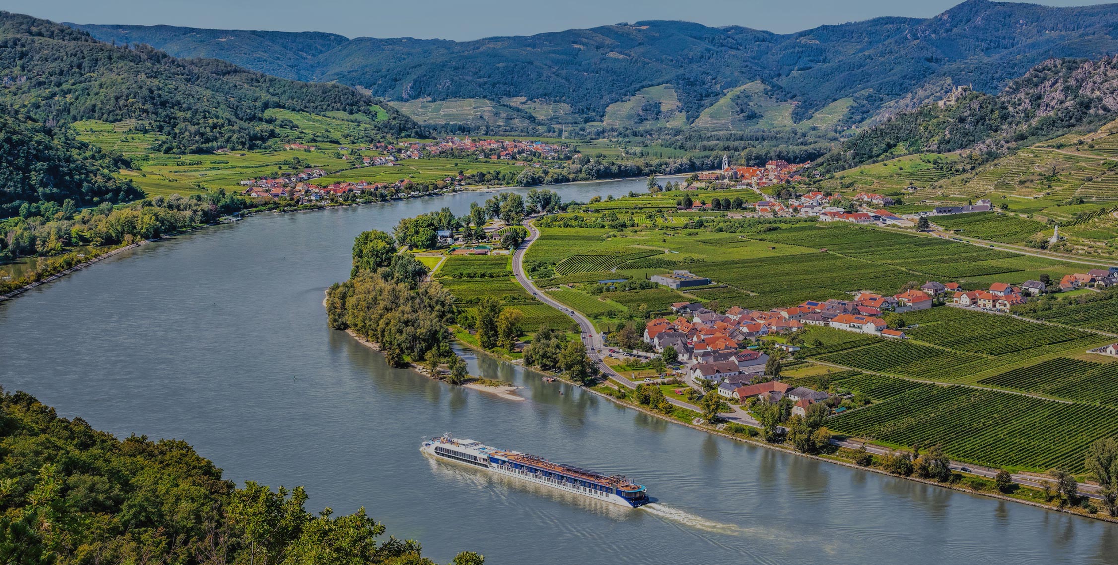 A scenic view of J Wrigley Vineyards along the river with lush vineyards and rolling hills in the background.