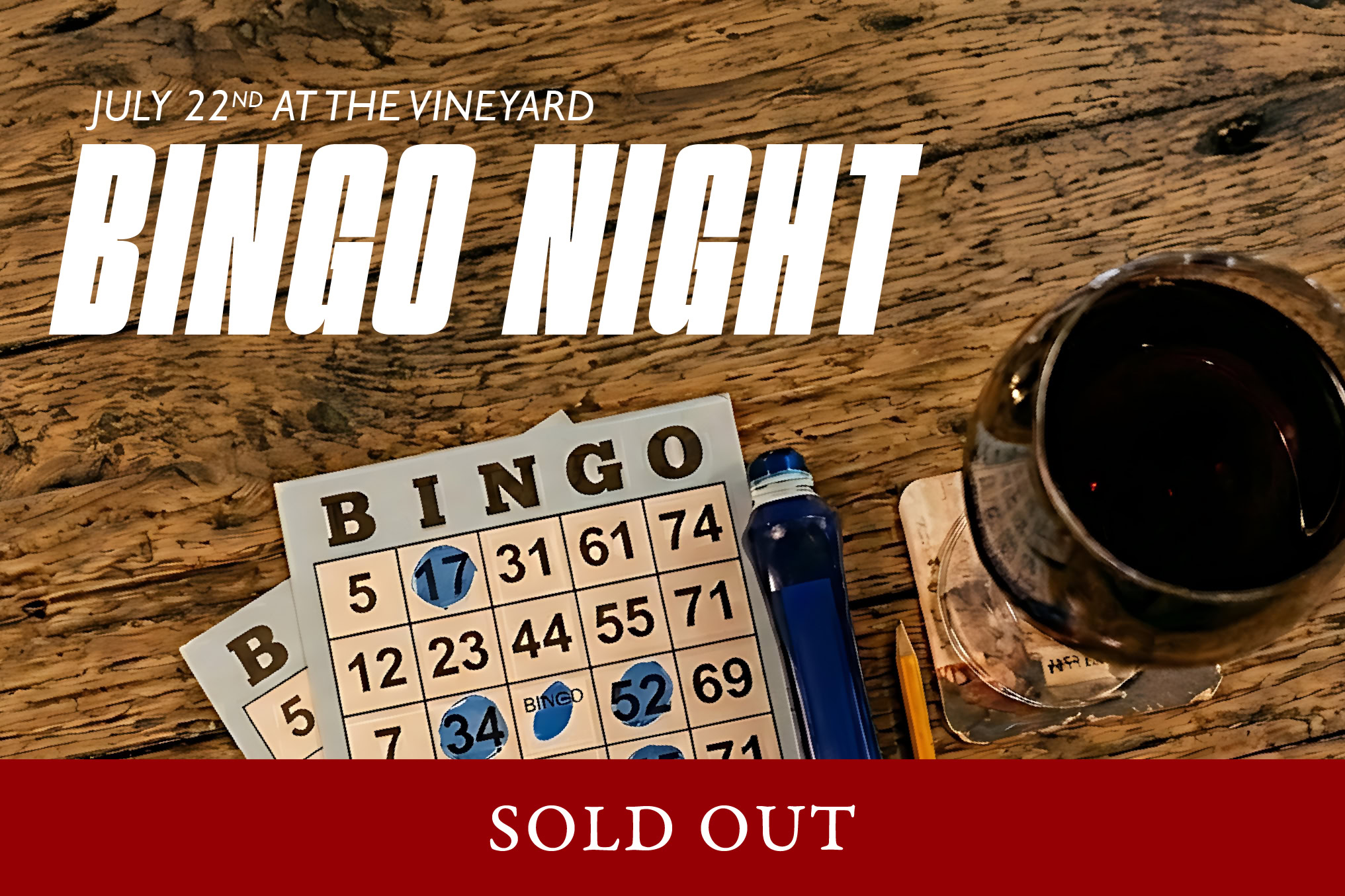 Bingo cards and a glass of red wine on a wooden table at J Wrigley Vineyards event.